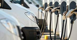 Fotografia de várias carrinhas brancas, lado a lado, em frente a vários postos de carregamento.