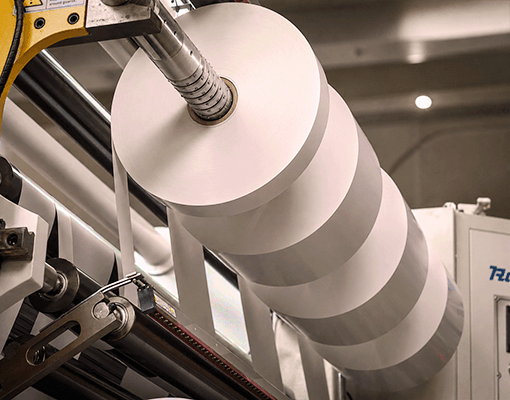 Bobinas de papel em linha de produção industrial. A imagem representa fabrico de papel, processos industriais contínuos e manutenção de equipamentos de produção.