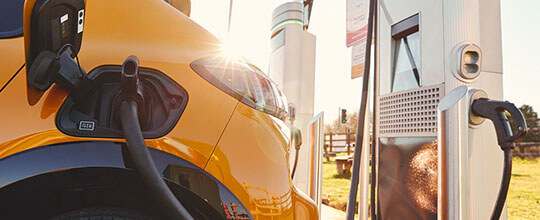 Fotografía de la parte trasera de un coche amarillo. Tiene la tapa de combustible abierta y un cargador insertado.