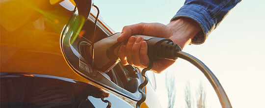 Fotografía en primer plano de una mano sosteniendo un cargador que se inserta en el tanque del automóvil.