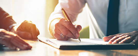Fotografía de primer plano de manos escribiendo en papel, sobre una mesa.
