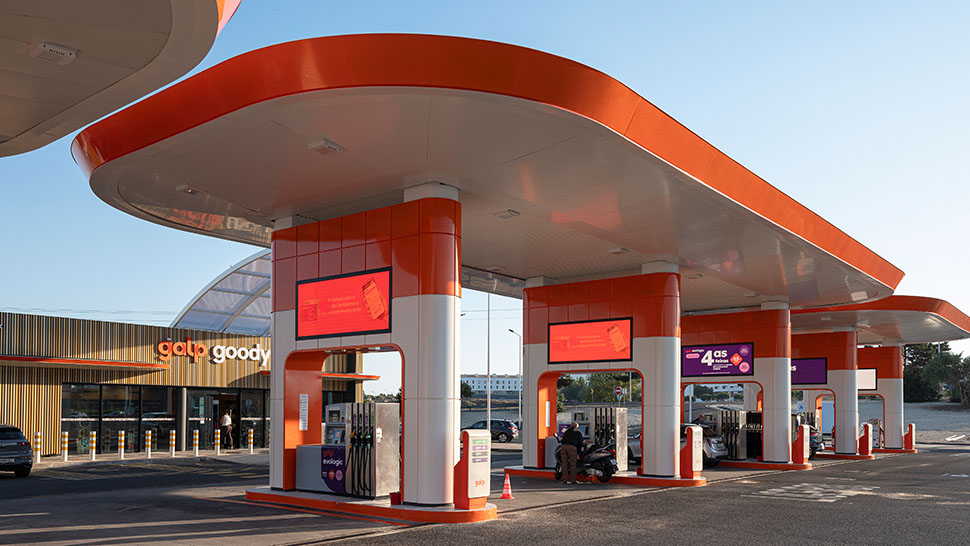 Estación de servicio Galp con varios surtidores bajo una marquesina naranja, con zona de tienda y vehículos repostando.
