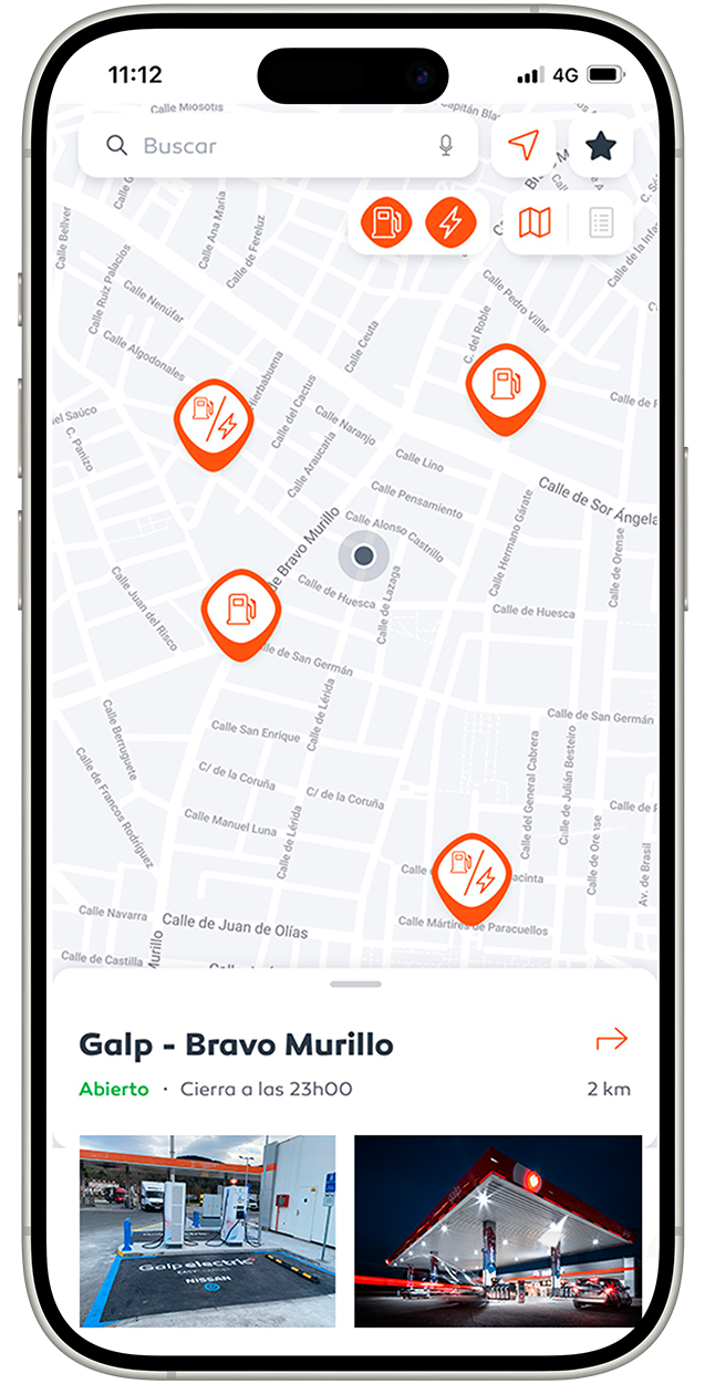 Pantalla con un mapa urbano en tonos claros que muestra varios puntos de recarga eléctrica señalados con iconos naranjas. En la parte superior hay una barra de búsqueda, acompañada de iconos de micrófono, ubicación, favoritos y mapa. En el mapa, un punto indica la posición del usuario. En la parte inferior, una tarjeta informativa del punto 'Galp - Bravo Murillo', con estado 'Abierto' y aviso de cierre, situado a 2 km. La tarjeta incluye dos imágenes: de un punto de carga eléctrica y de una estación Galp.
