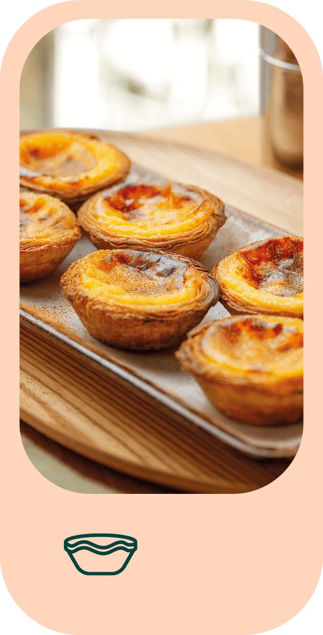 Fotografia em grande plano de uma travessa com seis pastéis de nata polvilhados com canela.