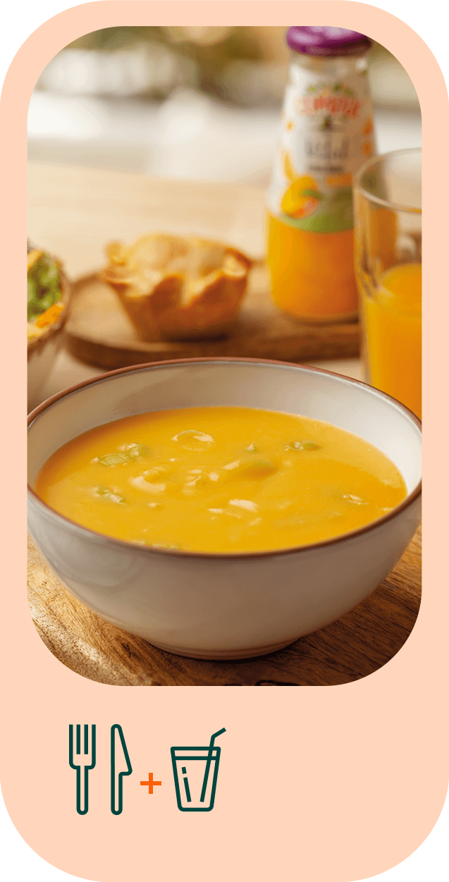 Fotografia em grande plano de uma tigela de sopa. Atrás é visível uma salada de alface e tomate, um copo de sumo e uma empada.